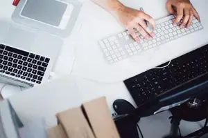 Person working at a desk with multiple electronic devices, including a laptop, desktop keyboard to check keyboard keys